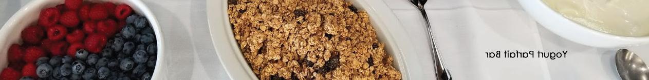 Yogurt Parfait Bar, pic with granola, raspberries, blueberries, and yogurt in bowls on a white tablecloth with spoon.